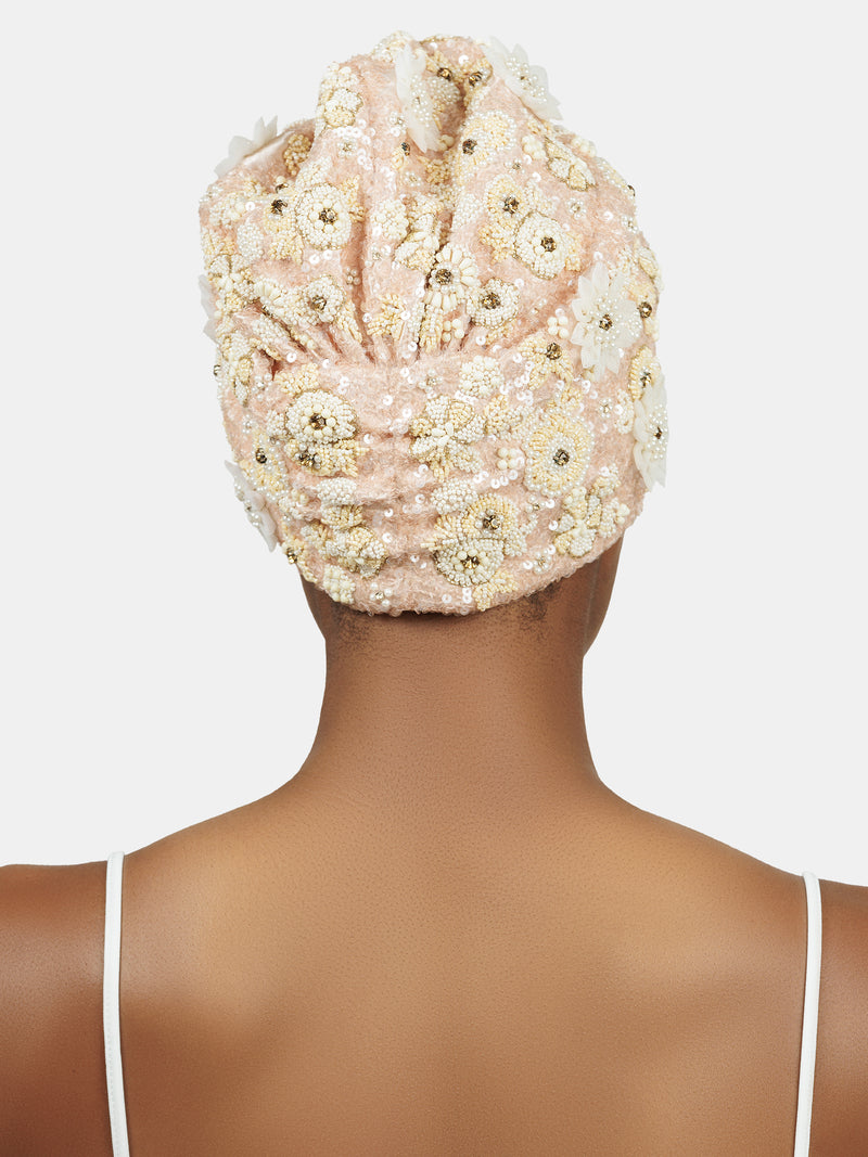 Back view of black female model wearing hand made sequin-embellished peach color turban with a tridimensional tonal flower pattern design by Maryjane Claverol